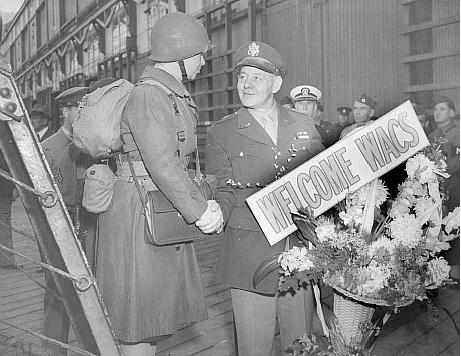 Army officer greets WACS with flowers in WWII.
